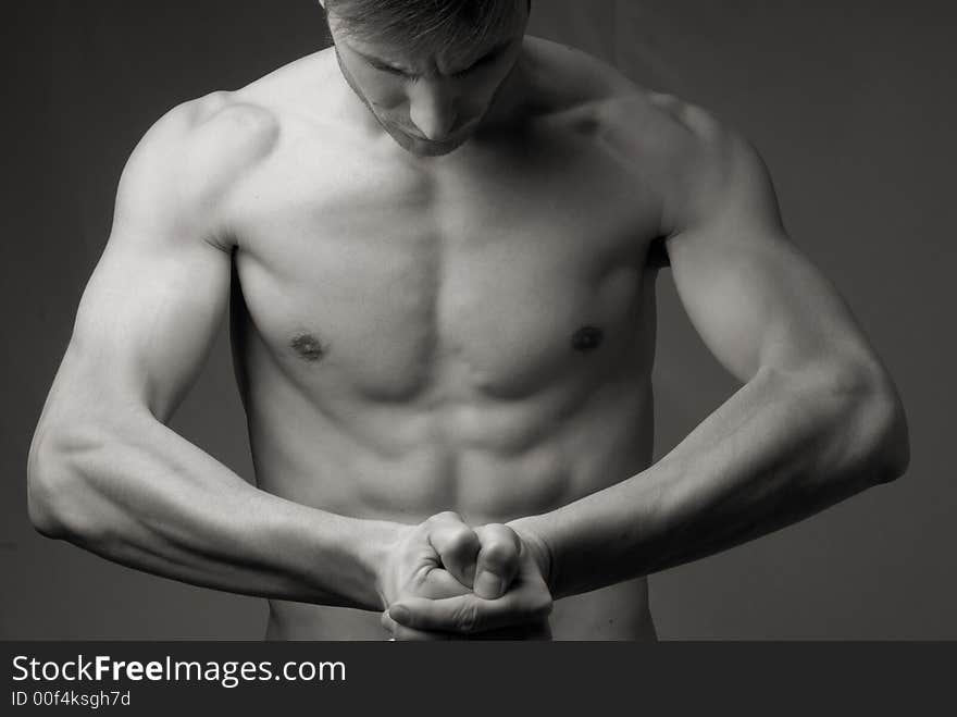 Young guy of an athletic constitution does sports exercises, strong pressure of muscles