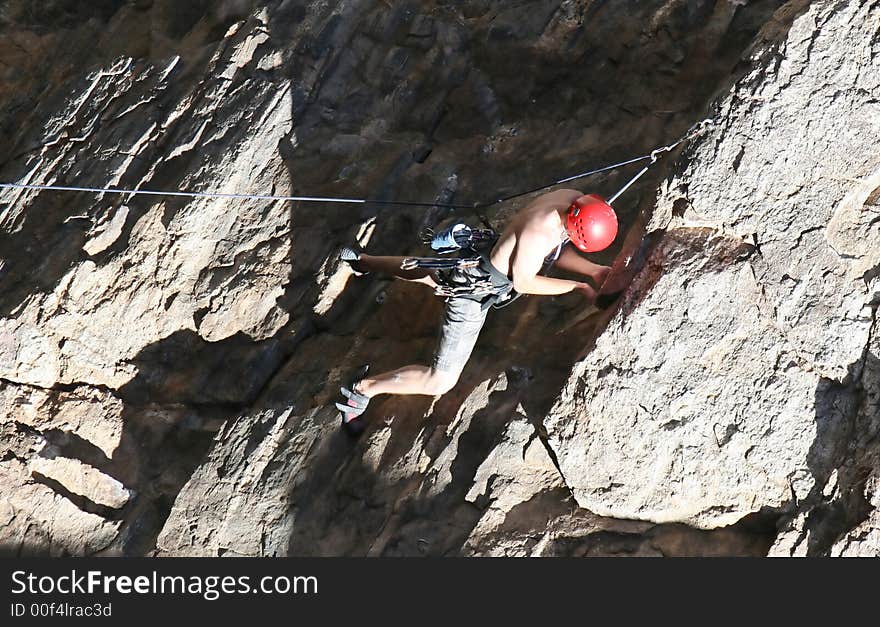 A rock climber works his way up a rock face protected by a rope clipped into bolts. He is wearing a helmet and quickdraws dangle from his harness. The route is in the desert southwest United States. Mt Lemmon, Arizona. A rock climber works his way up a rock face protected by a rope clipped into bolts. He is wearing a helmet and quickdraws dangle from his harness. The route is in the desert southwest United States. Mt Lemmon, Arizona.