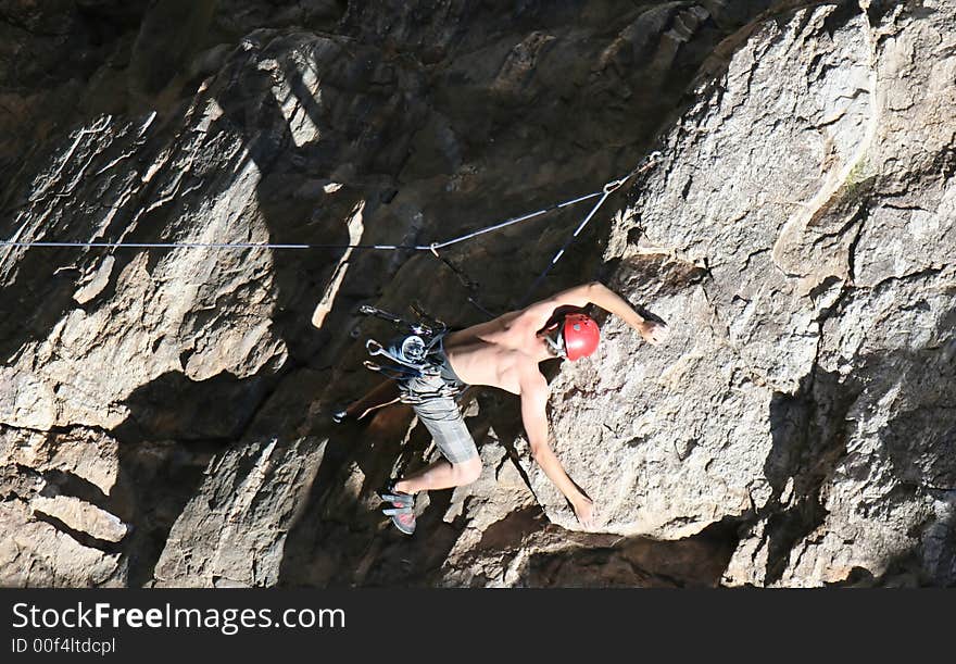 A rock climber works his way up a rock face protected by a rope clipped into bolts. He is wearing a helmet and quickdraws dangle from his harness. The route is in the desert southwest United States. Mt Lemmon, Arizona. A rock climber works his way up a rock face protected by a rope clipped into bolts. He is wearing a helmet and quickdraws dangle from his harness. The route is in the desert southwest United States. Mt Lemmon, Arizona.