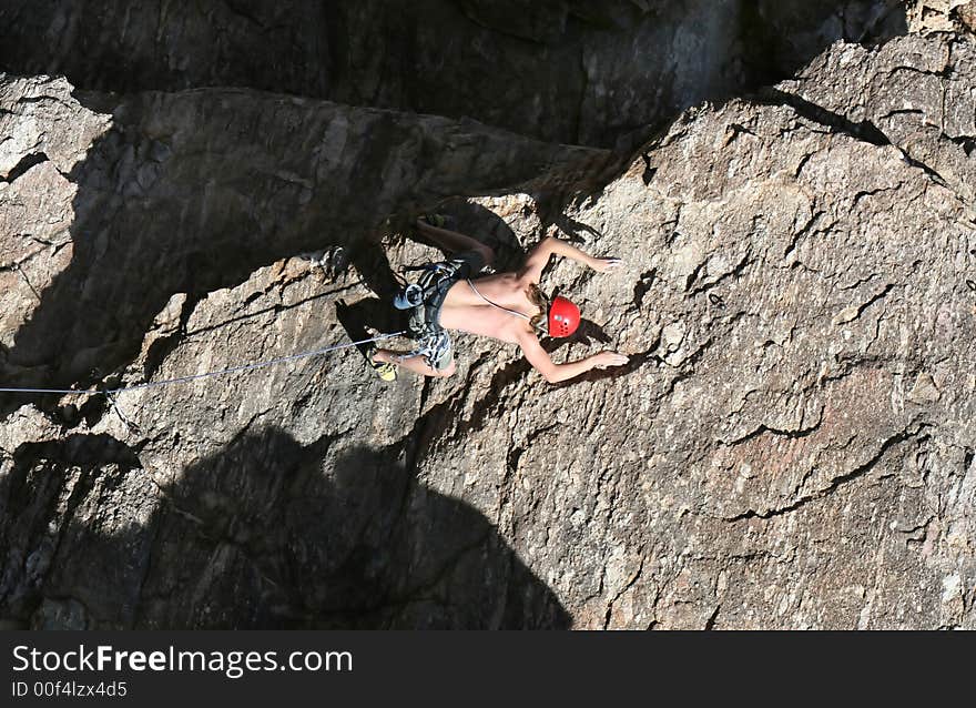 A rock climber works his way up a rock face protected by a rope clipped into bolts. He is wearing a helmet and quickdraws dangle from his harness. The route is in the desert southwest United States. Mt Lemmon, Arizona. A rock climber works his way up a rock face protected by a rope clipped into bolts. He is wearing a helmet and quickdraws dangle from his harness. The route is in the desert southwest United States. Mt Lemmon, Arizona.