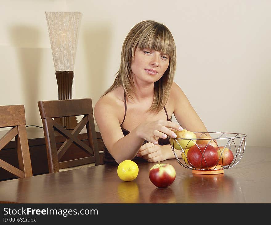 Attractive blond girl siting at the table with apples in a basket. Attractive blond girl siting at the table with apples in a basket