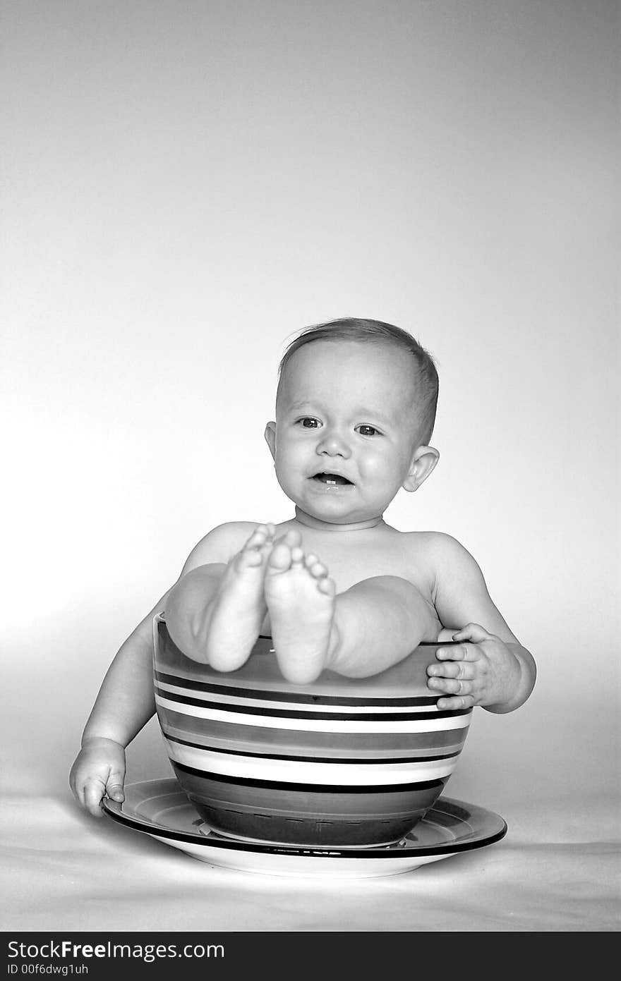 Black and white image of an adorable baby sitting in an over-sized teacup. Black and white image of an adorable baby sitting in an over-sized teacup