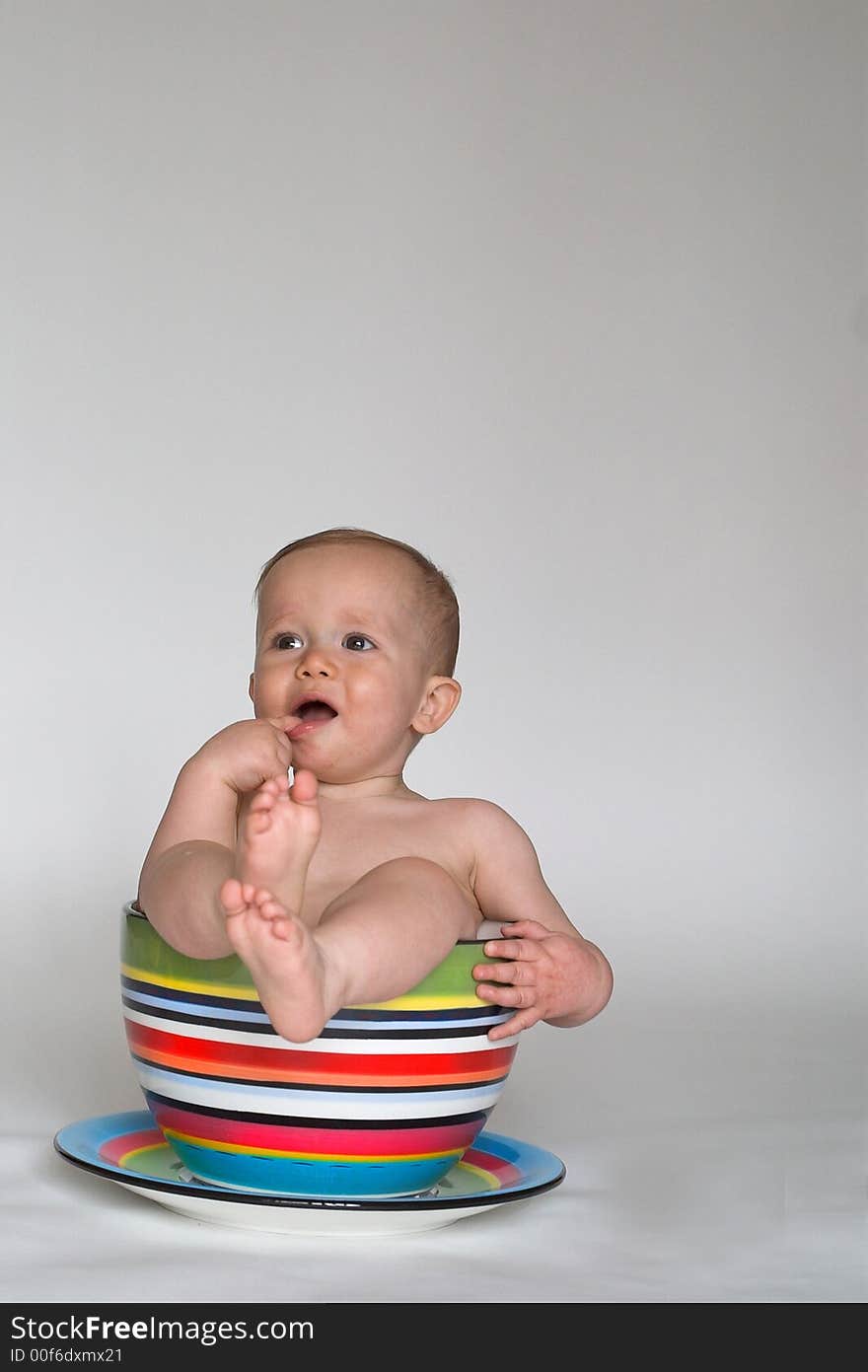 Image of an adorable baby sitting in a colorful, over-sized teacup. Image of an adorable baby sitting in a colorful, over-sized teacup