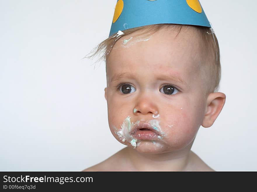 Image of an adorable 1 year old, wearing a paper hat, with cake frosting all over his face. Image of an adorable 1 year old, wearing a paper hat, with cake frosting all over his face