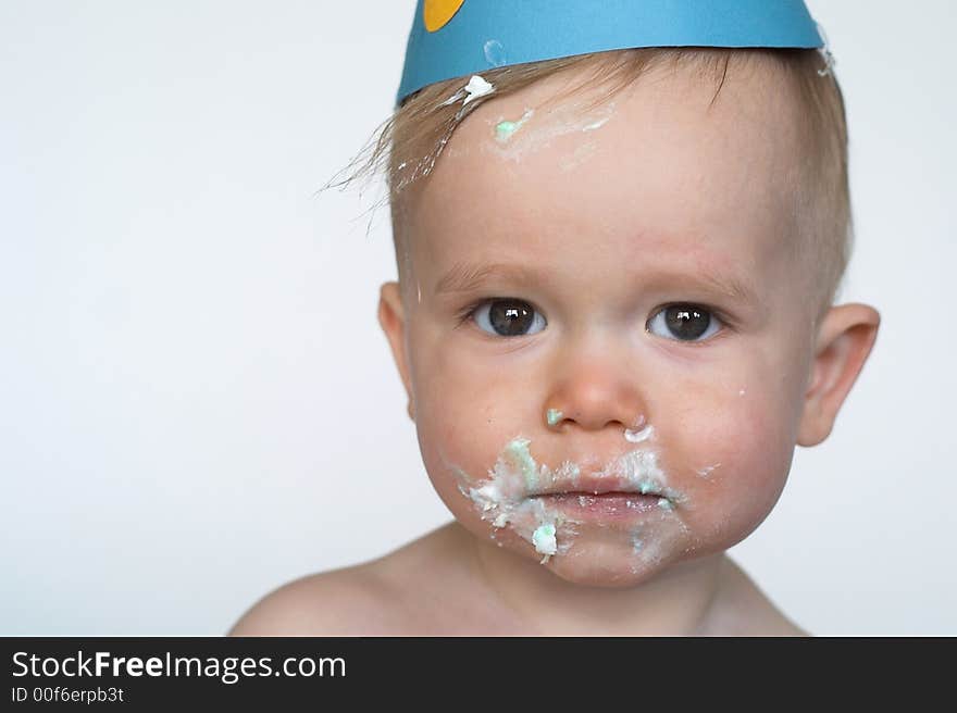 Image of an adorable 1 year old, wearing a paper hat, with cake frosting all over his face. Image of an adorable 1 year old, wearing a paper hat, with cake frosting all over his face