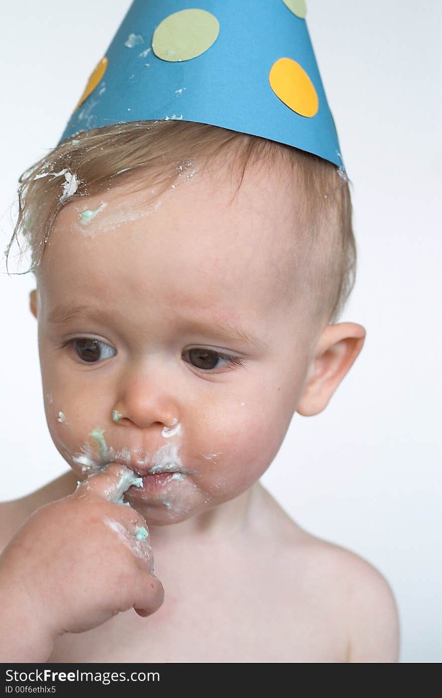 Image of an adorable 1 year old, wearing a paper hat, eating birthday cake. Image of an adorable 1 year old, wearing a paper hat, eating birthday cake