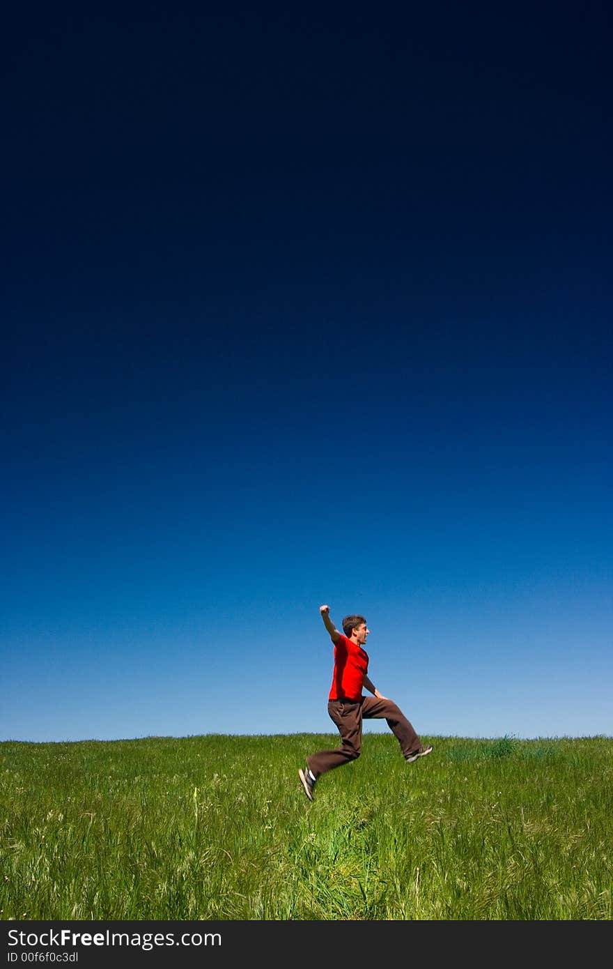 Active happy young man jumping in a green field against a clear blue sky. Active happy young man jumping in a green field against a clear blue sky