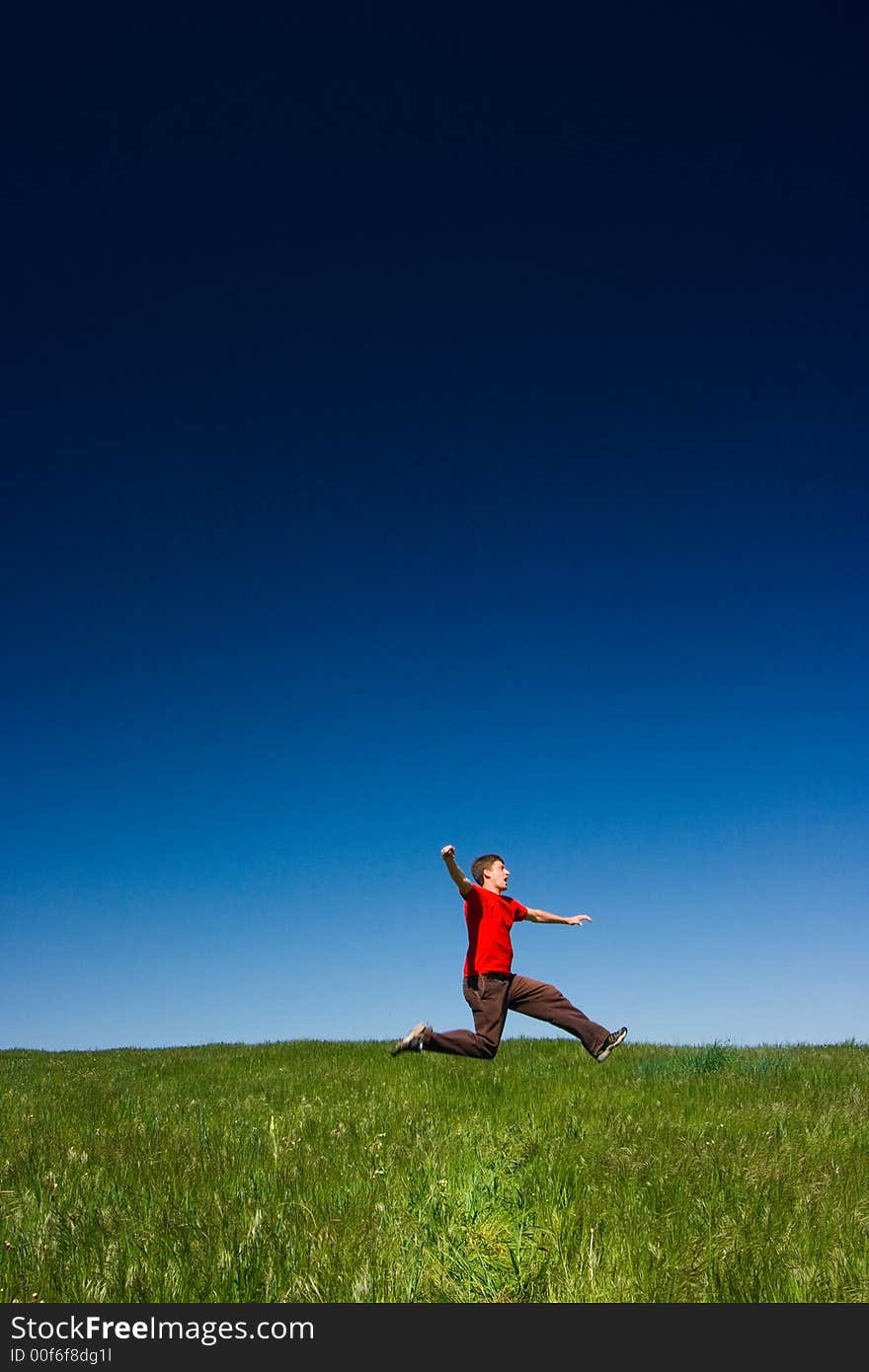 Active happy young man jumping in a green field against a clear blue sky. Active happy young man jumping in a green field against a clear blue sky