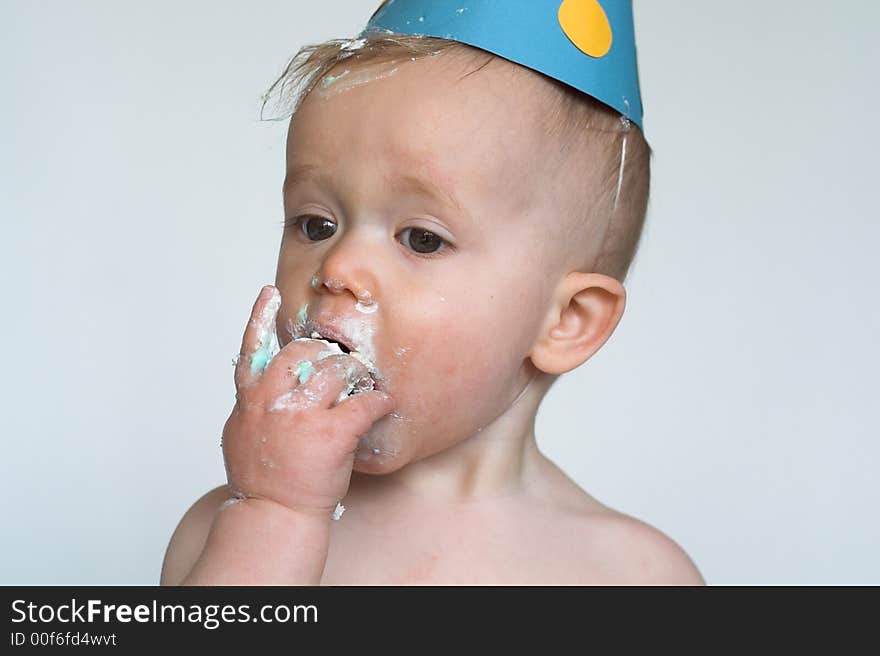 Image of an adorable 1 year old, wearing a paper hat, eating birthday cake. Image of an adorable 1 year old, wearing a paper hat, eating birthday cake