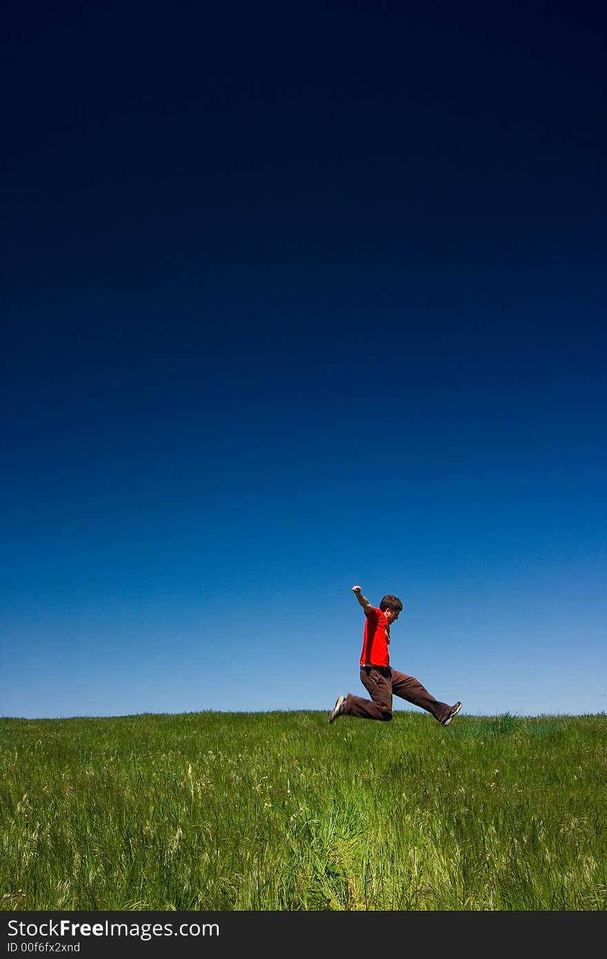 Active happy young man jumping in a green field against a clear blue sky. Active happy young man jumping in a green field against a clear blue sky