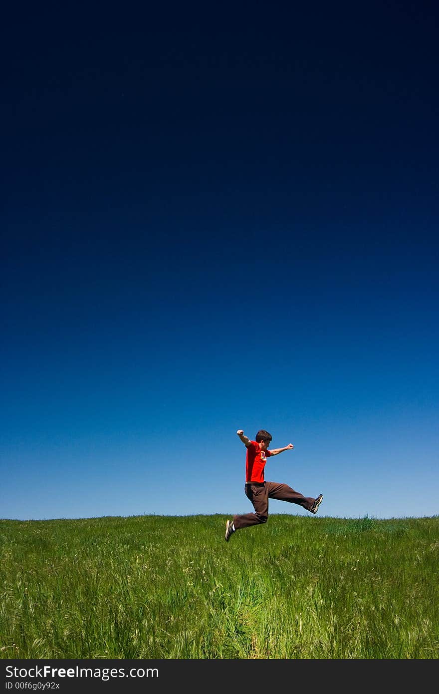 Active happy young man jumping in a green field against a clear blue sky. Active happy young man jumping in a green field against a clear blue sky