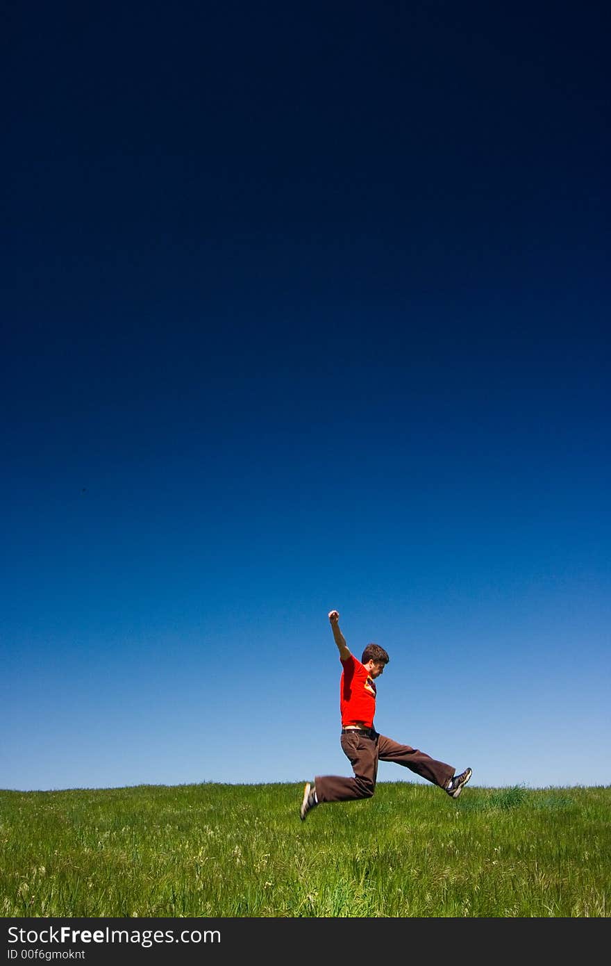 Active happy young man jumping in a green field against a clear blue sky. Active happy young man jumping in a green field against a clear blue sky