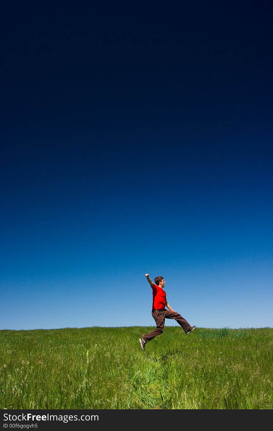 Active happy young man jumping in a green field against a clear blue sky. Active happy young man jumping in a green field against a clear blue sky