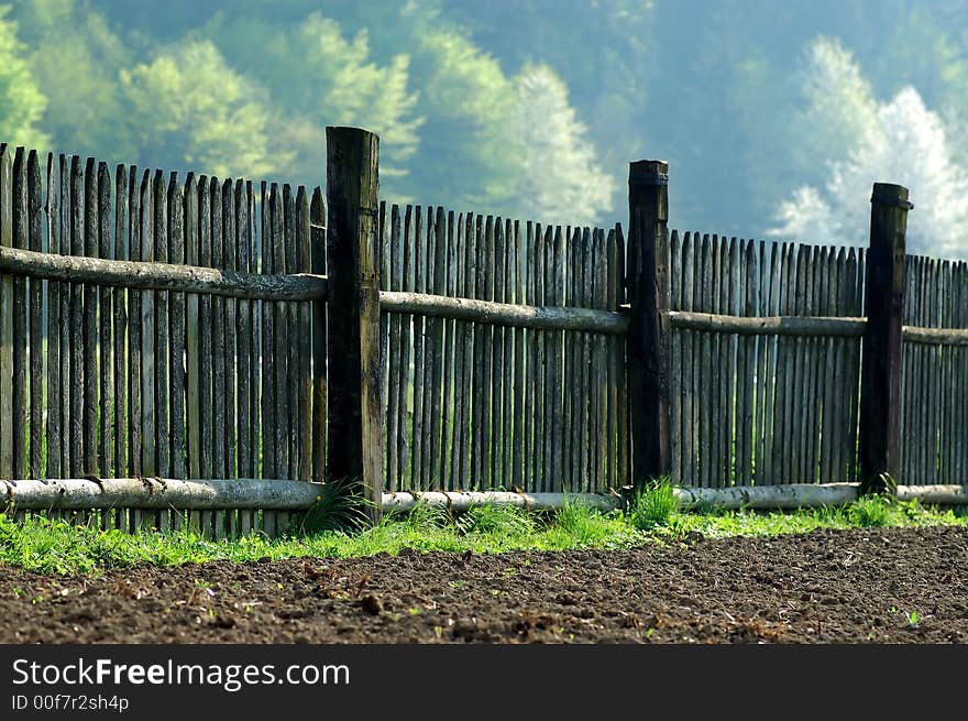 Old fence in the midst of brown field and trees