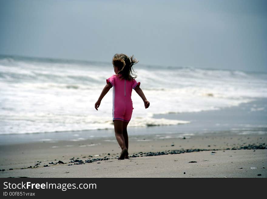 Portrait of a little girl walking towards the sea in a pink bathing suit