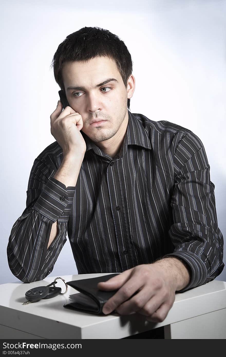 Serious young man with car keys and wallet speaking phone. Serious young man with car keys and wallet speaking phone