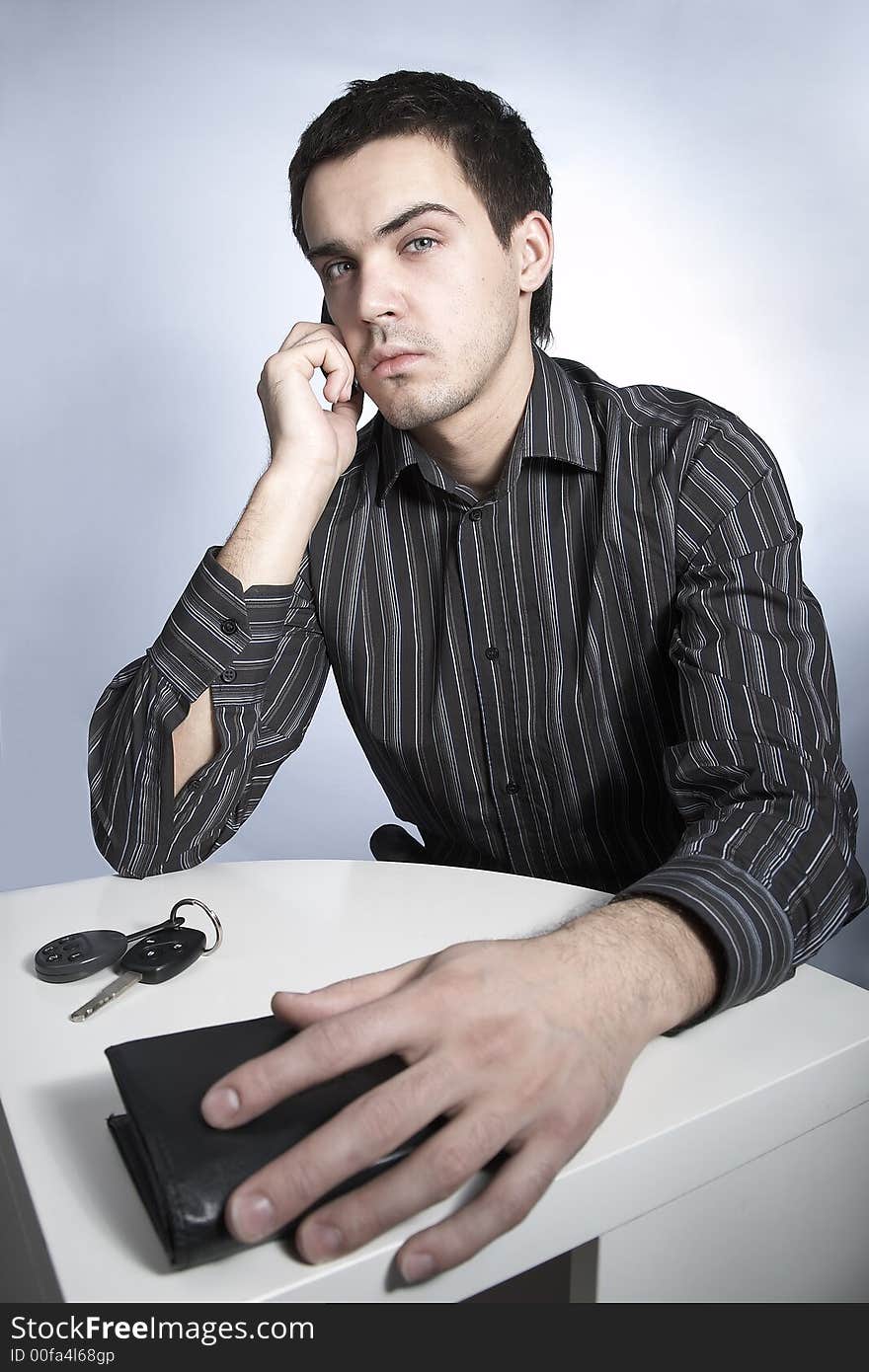 Serious young man with car keys and wallet speaking phone. Serious young man with car keys and wallet speaking phone