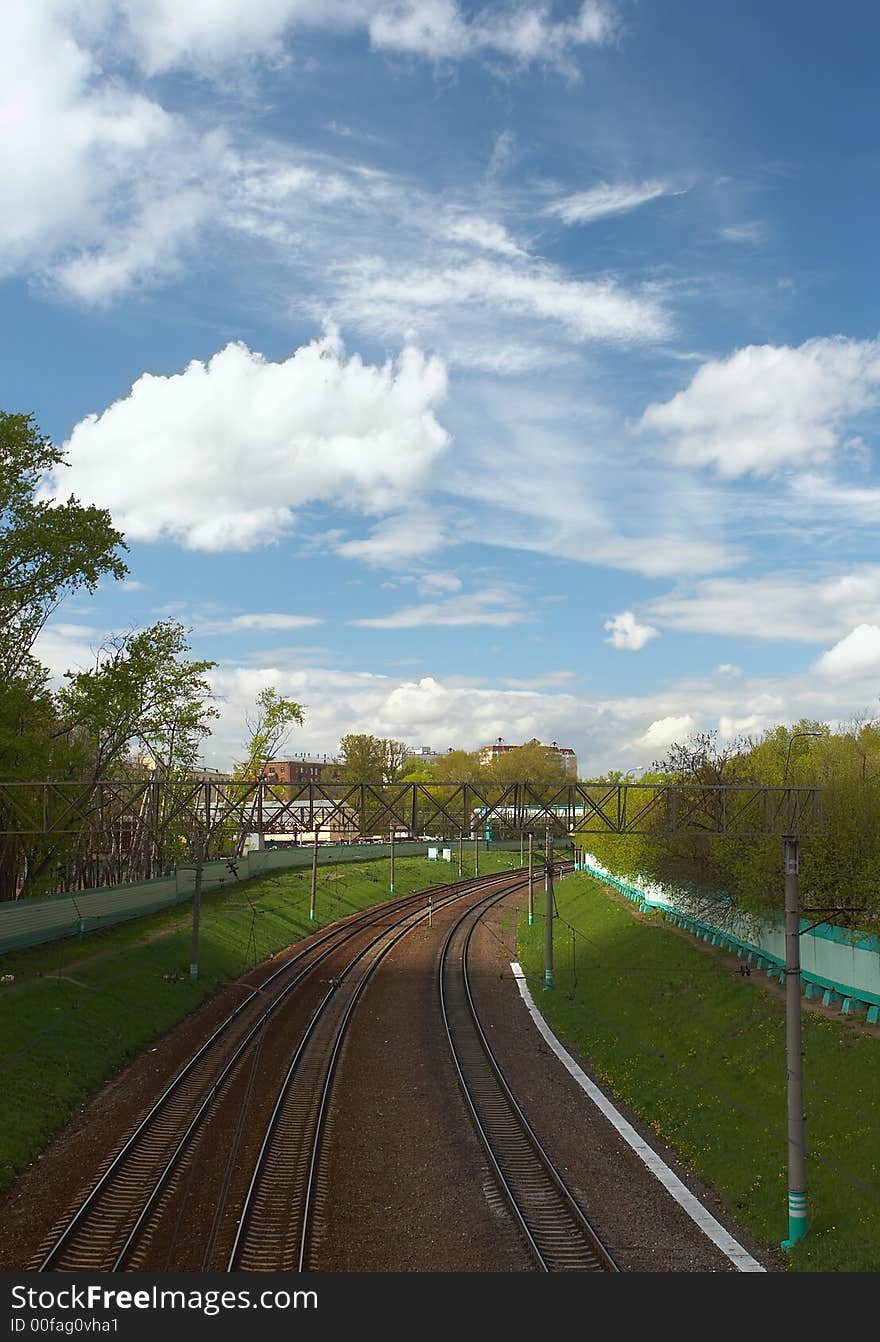 Kind on the railway with a green grass on each side and the beautiful sky with clouds