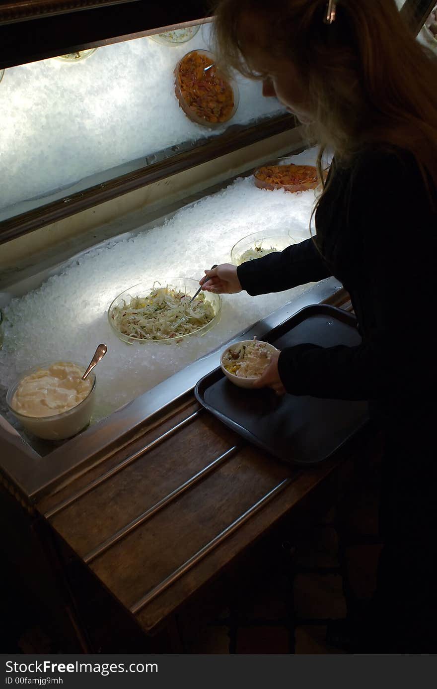 The girl lays down salad in a plate from the big bowl. The girl lays down salad in a plate from the big bowl