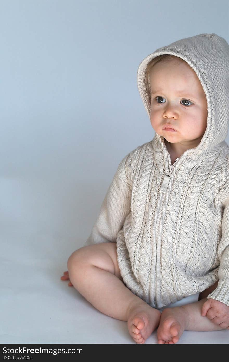 Image of cute baby wearing a hooded sweater, sitting in front of a white background. Image of cute baby wearing a hooded sweater, sitting in front of a white background