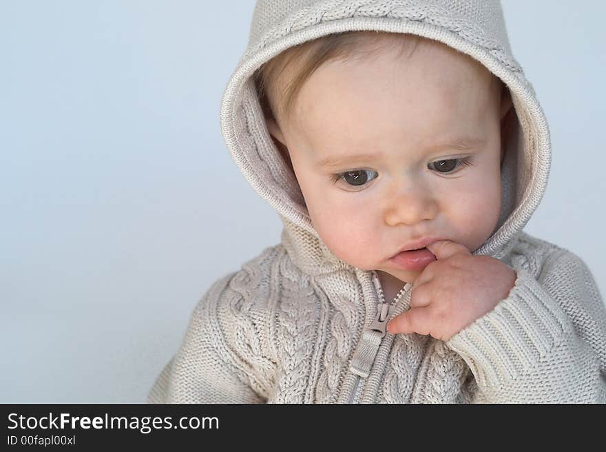 Image of cute baby wearing a hooded sweater, sitting in front of a white background. Image of cute baby wearing a hooded sweater, sitting in front of a white background