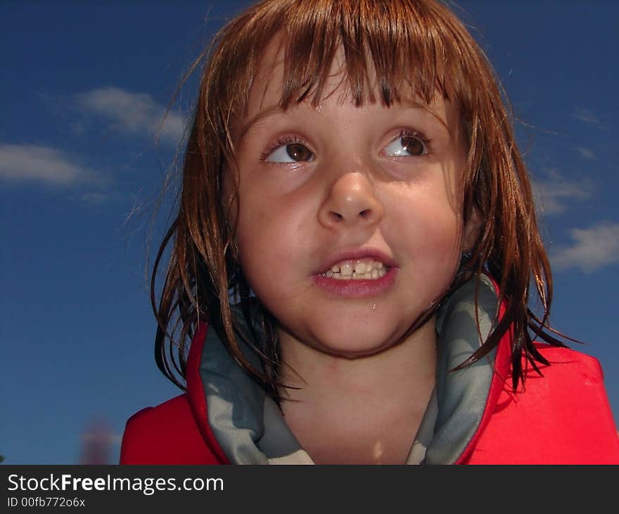 Color photo close up of little girl against blue sky, wearing lifejacket. Still a little wet from being in lake. Color photo close up of little girl against blue sky, wearing lifejacket. Still a little wet from being in lake.