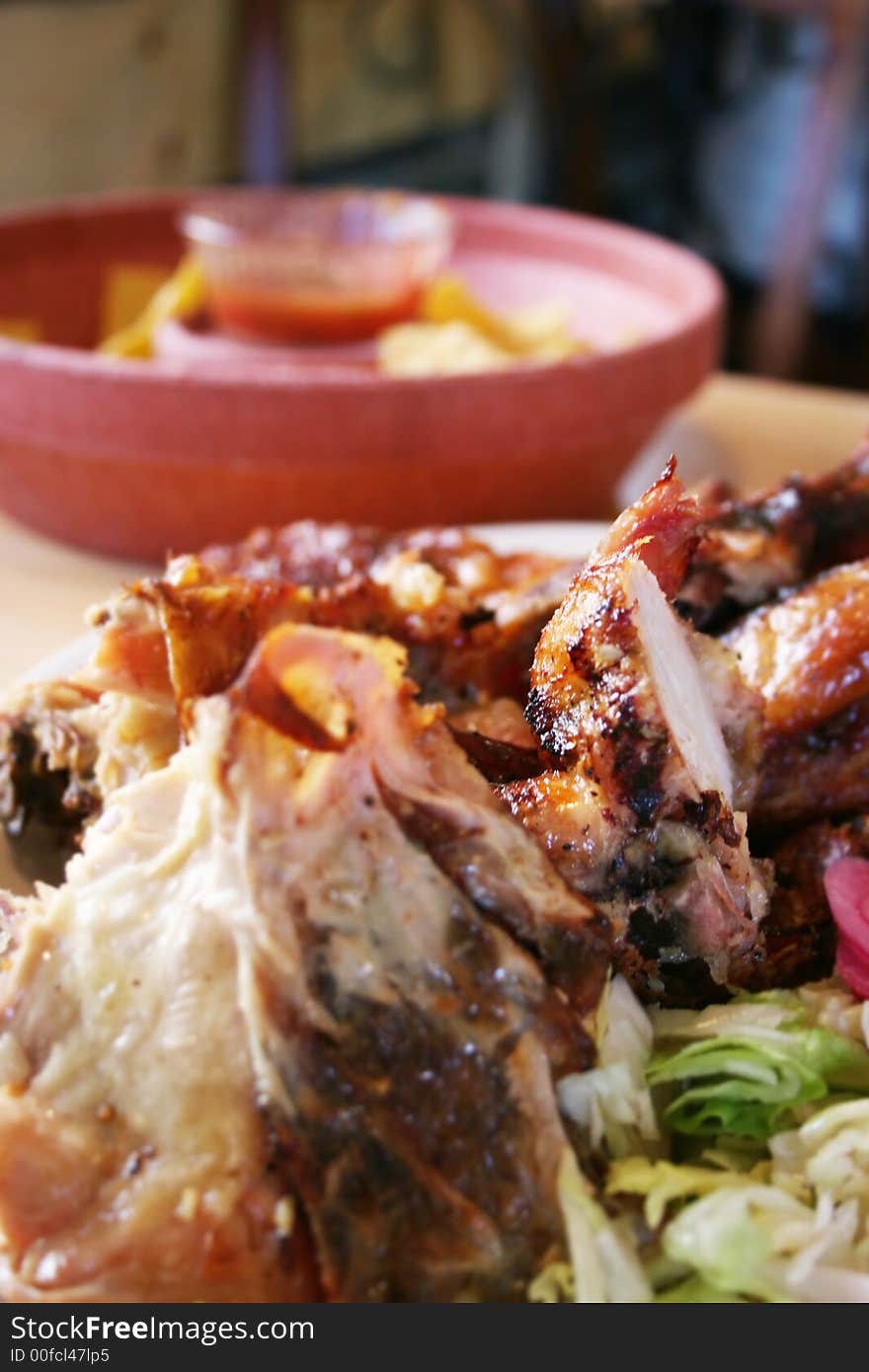 Chips and Salsa are on the table in a restaurant with chicken in the foreground ready to be eatin in the dinner. Chips and Salsa are on the table in a restaurant with chicken in the foreground ready to be eatin in the dinner