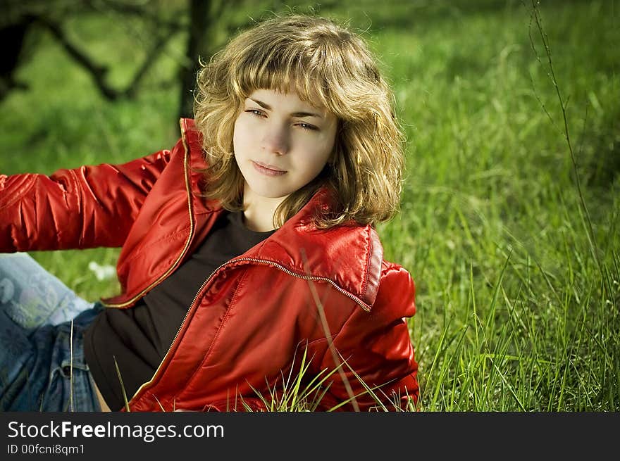 Young pretty blond wearing red jacket sitting on the green grass. Young pretty blond wearing red jacket sitting on the green grass