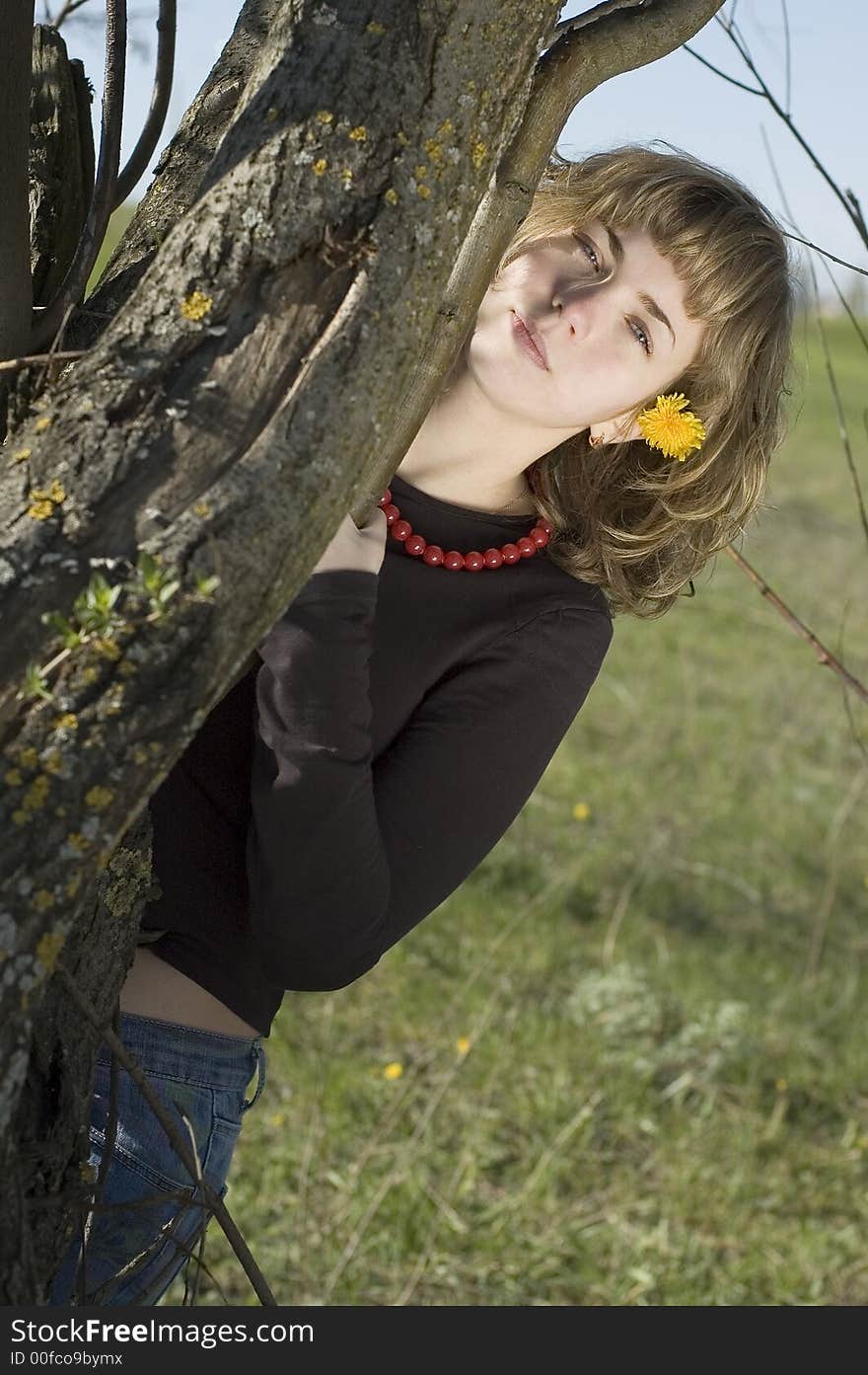 Pretty blond with a dandelion standing near a tree