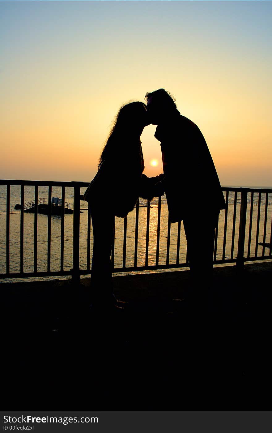 Silhouette couple kissing at sunset by the coast. Silhouette couple kissing at sunset by the coast