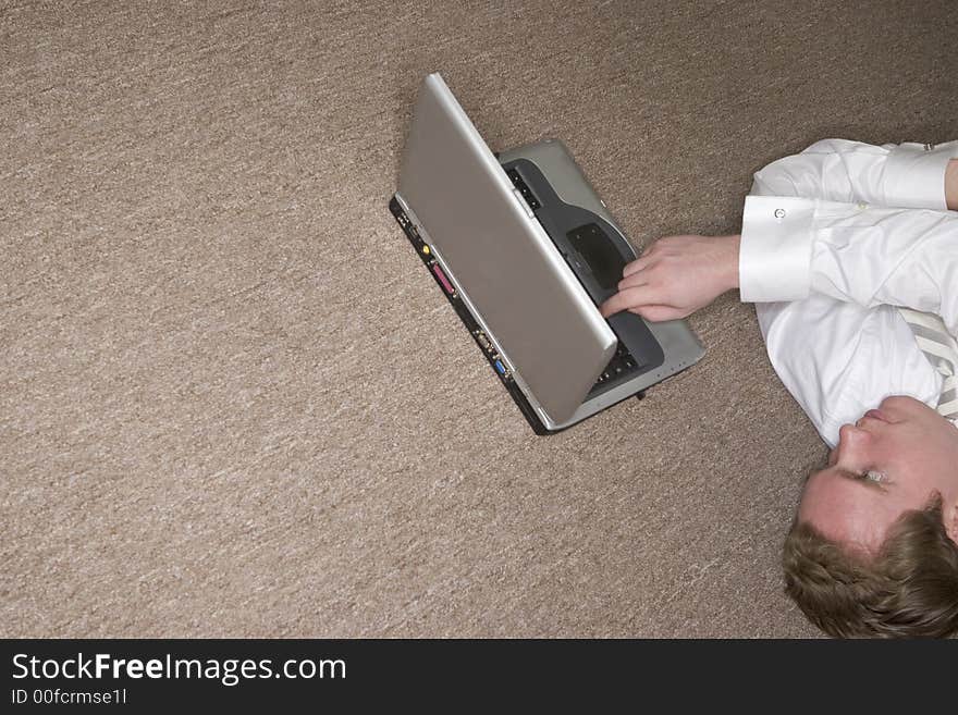 Businessman tired and stressed uses his laptop with one finger while lying on the floor. Businessman tired and stressed uses his laptop with one finger while lying on the floor