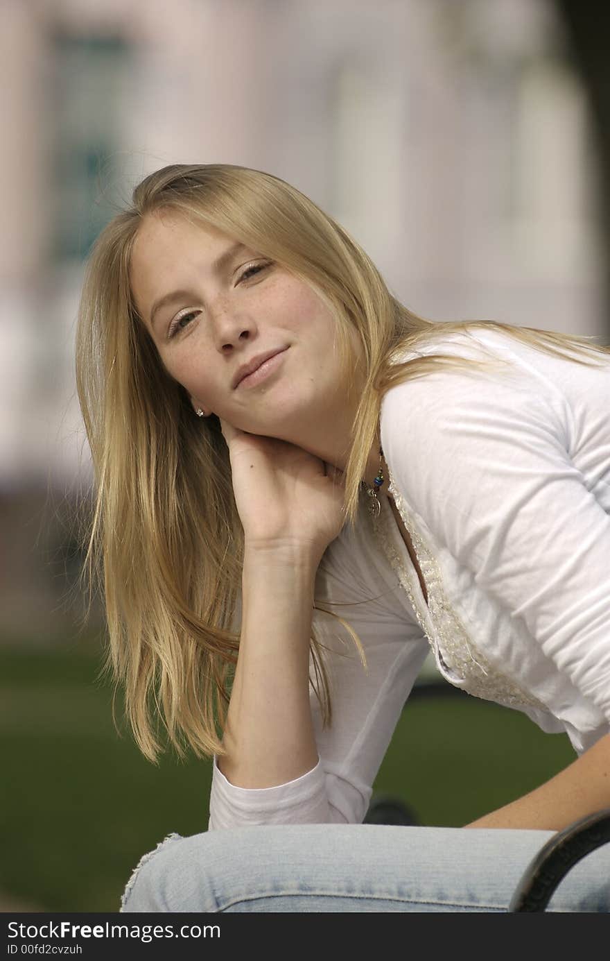 A caucasian female American teenager sits on a park bench on the Square in a small Texas town.