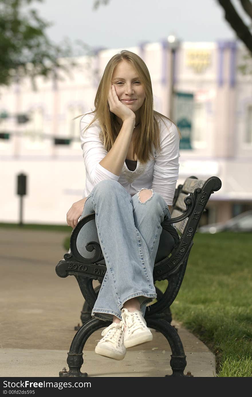 A caucasian female American teenager sits on a park bench on the Square in a small Texas town.