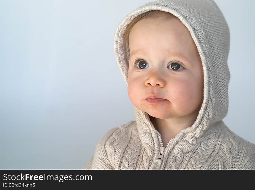 Image of cute baby wearing a hooded sweater, sitting in front of a white background. Image of cute baby wearing a hooded sweater, sitting in front of a white background