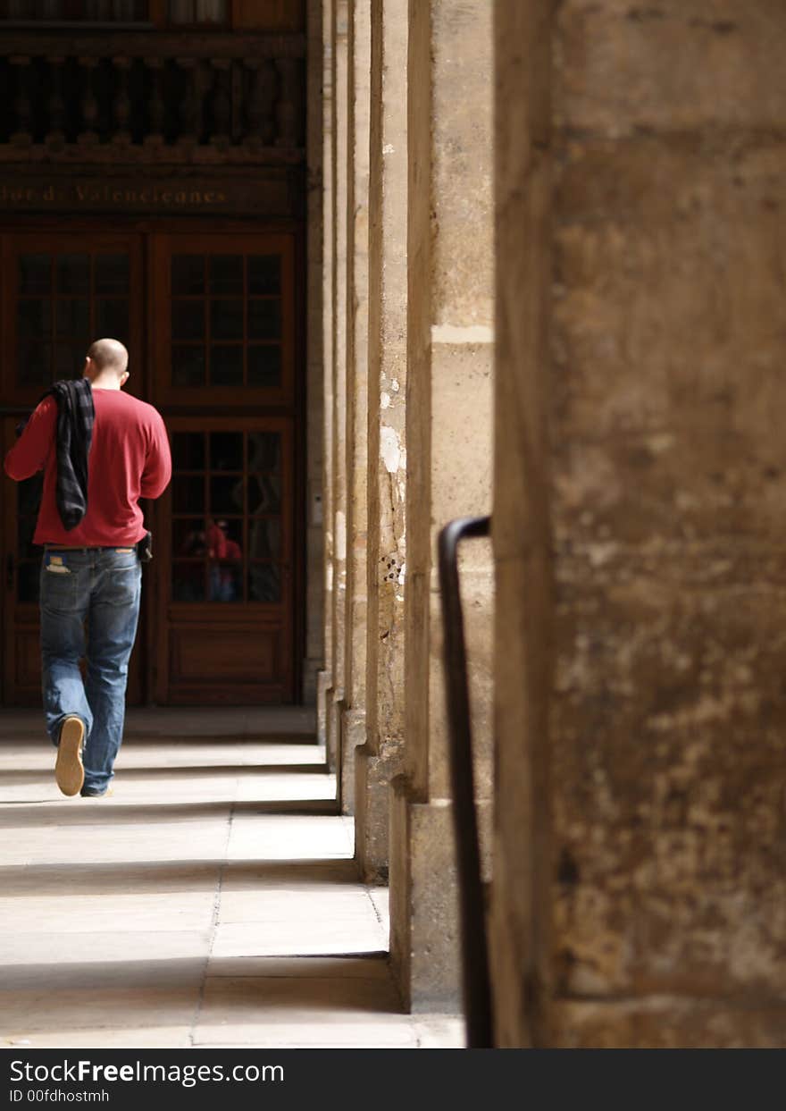 A man walking down a row of columns in sunlight.