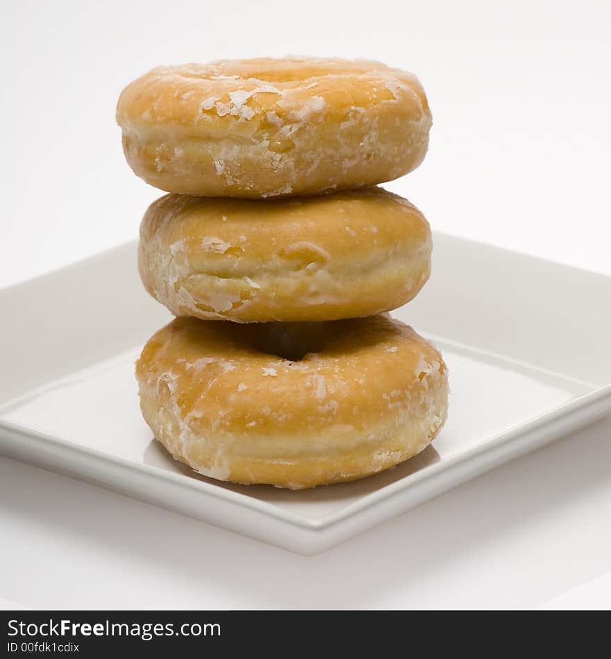 Three glazed donuts stacked on white plate