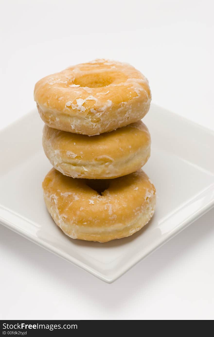 Three glazed donuts stacked on white plate