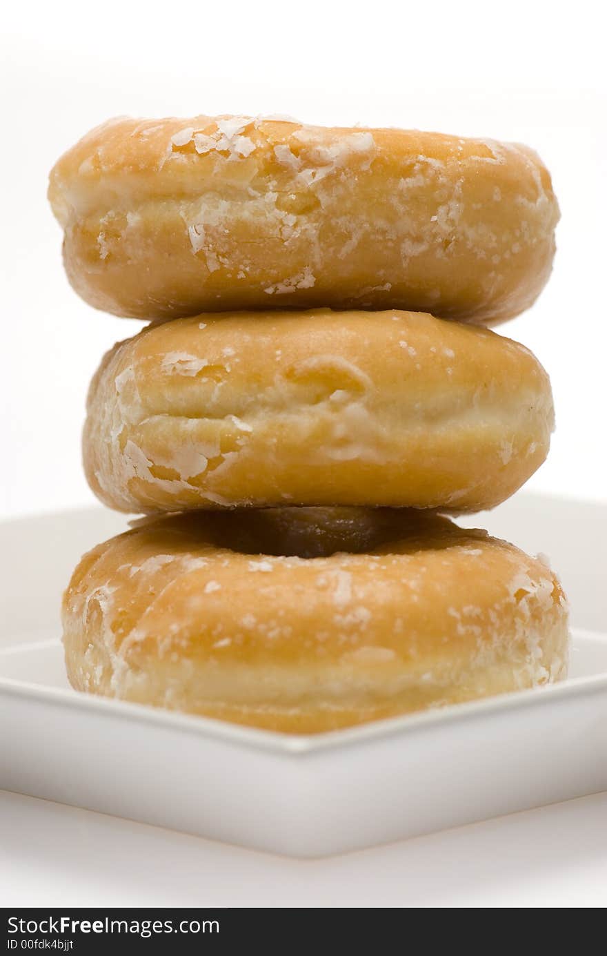 Three glazed donuts stacked on white plate side view