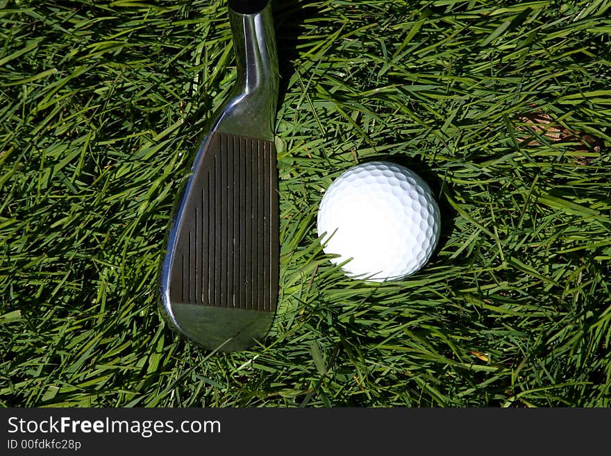 A golf club ready to strike a golf ball on the grass. A golf club ready to strike a golf ball on the grass