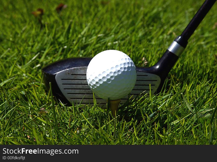 A golf club ready to strike a golf ball on the grass. A golf club ready to strike a golf ball on the grass