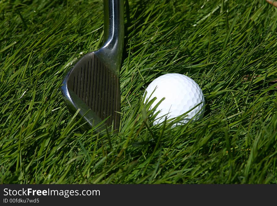 A golf club ready to strike a golf ball on the grass. A golf club ready to strike a golf ball on the grass