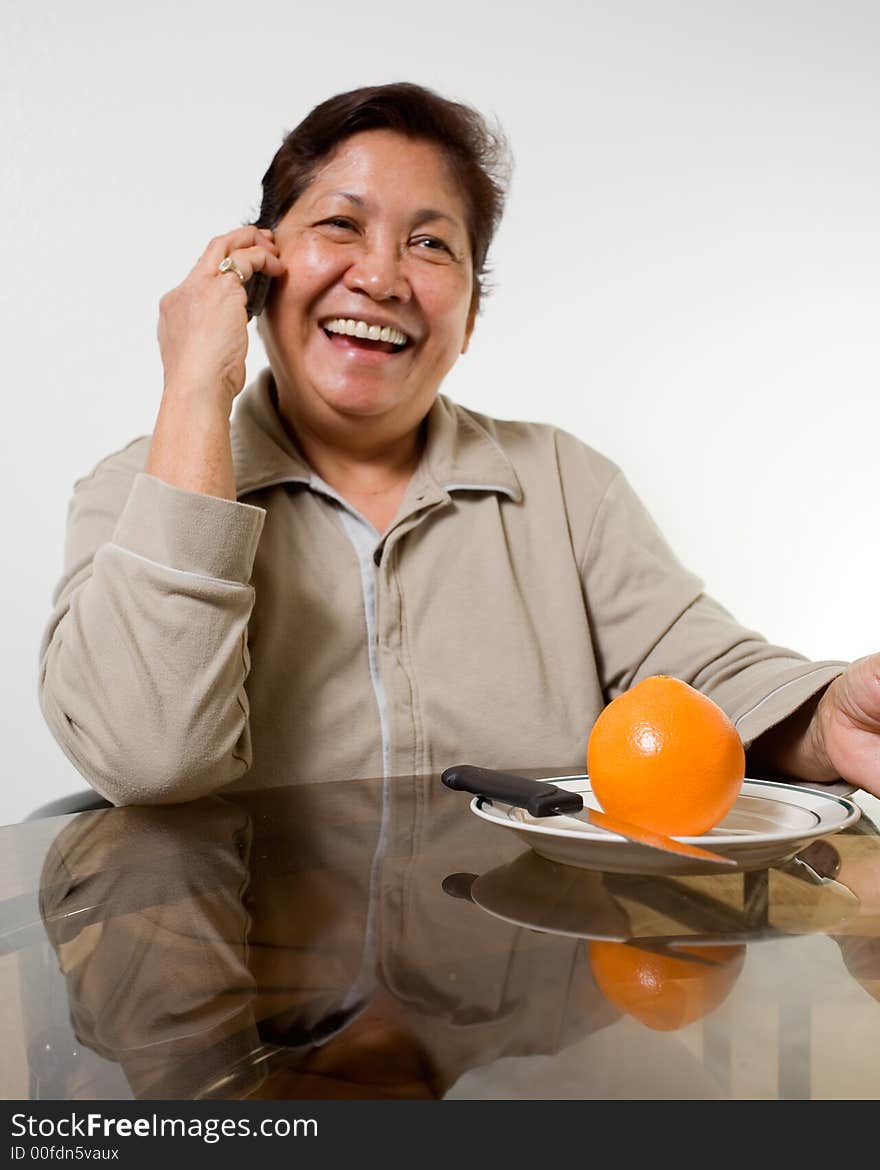 Portrait of a senior asian woman smiling sitting at the kitchen table about to peel and orange. Portrait of a senior asian woman smiling sitting at the kitchen table about to peel and orange