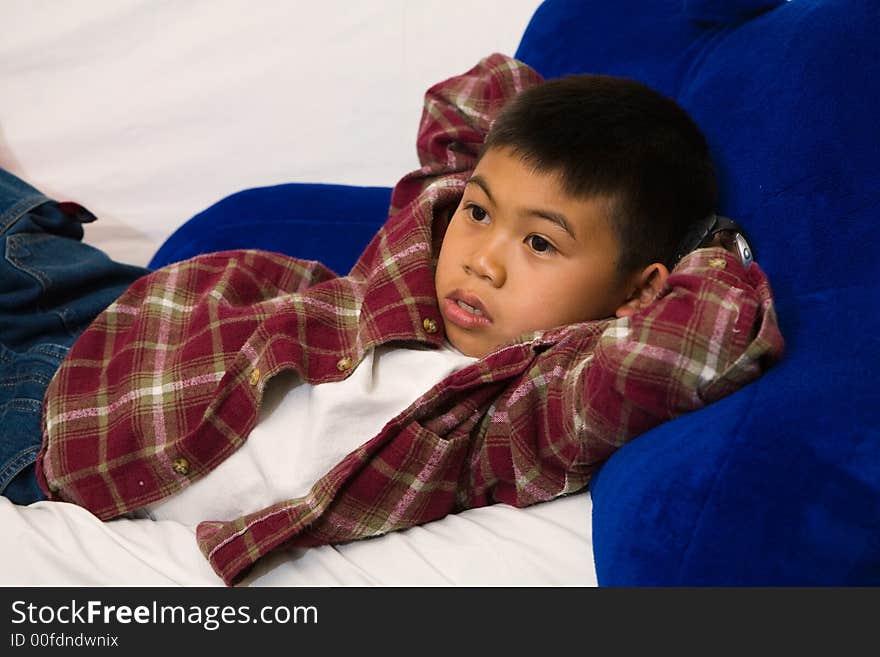 Young asian boy laying down on a sofa while looking engrossed in the television. Young asian boy laying down on a sofa while looking engrossed in the television