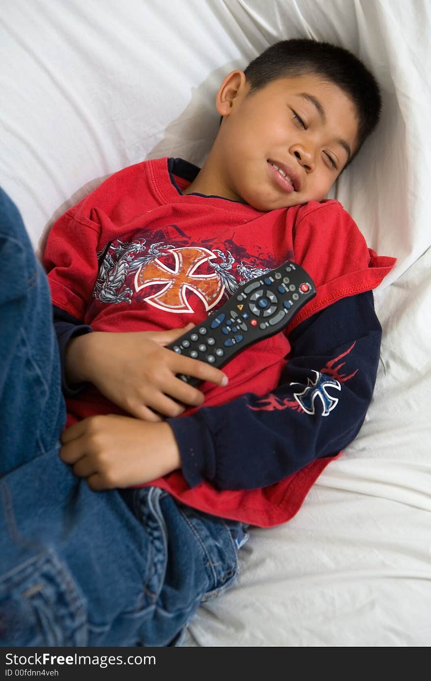 Young asian boy comfortably laying down on the sofa holding the television remote control. Young asian boy comfortably laying down on the sofa holding the television remote control