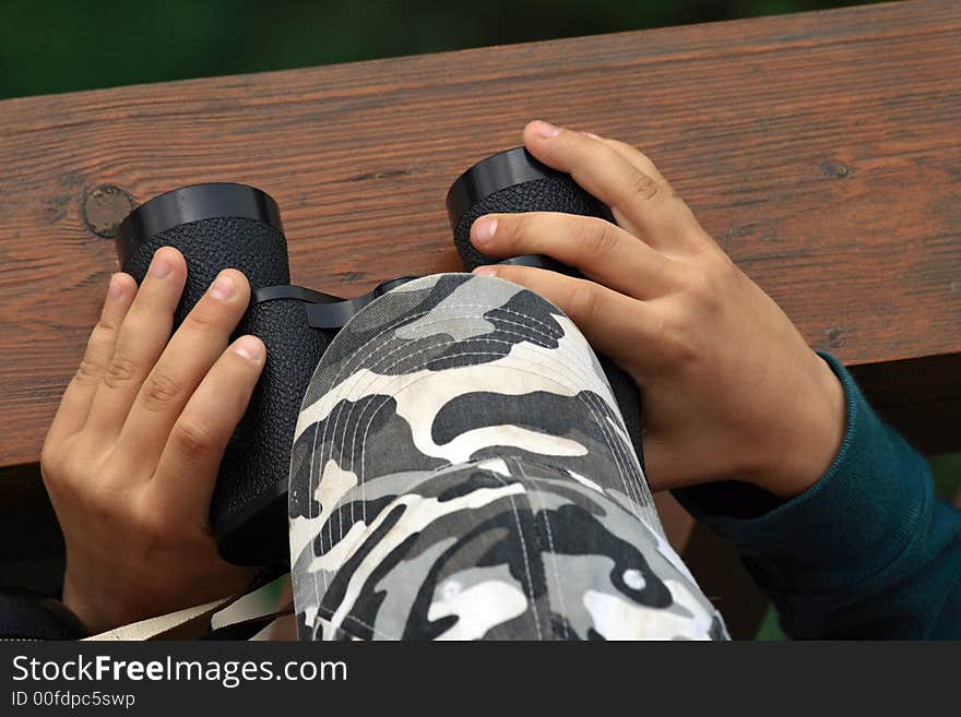 Child hands keep black binoculars on outlook-tower