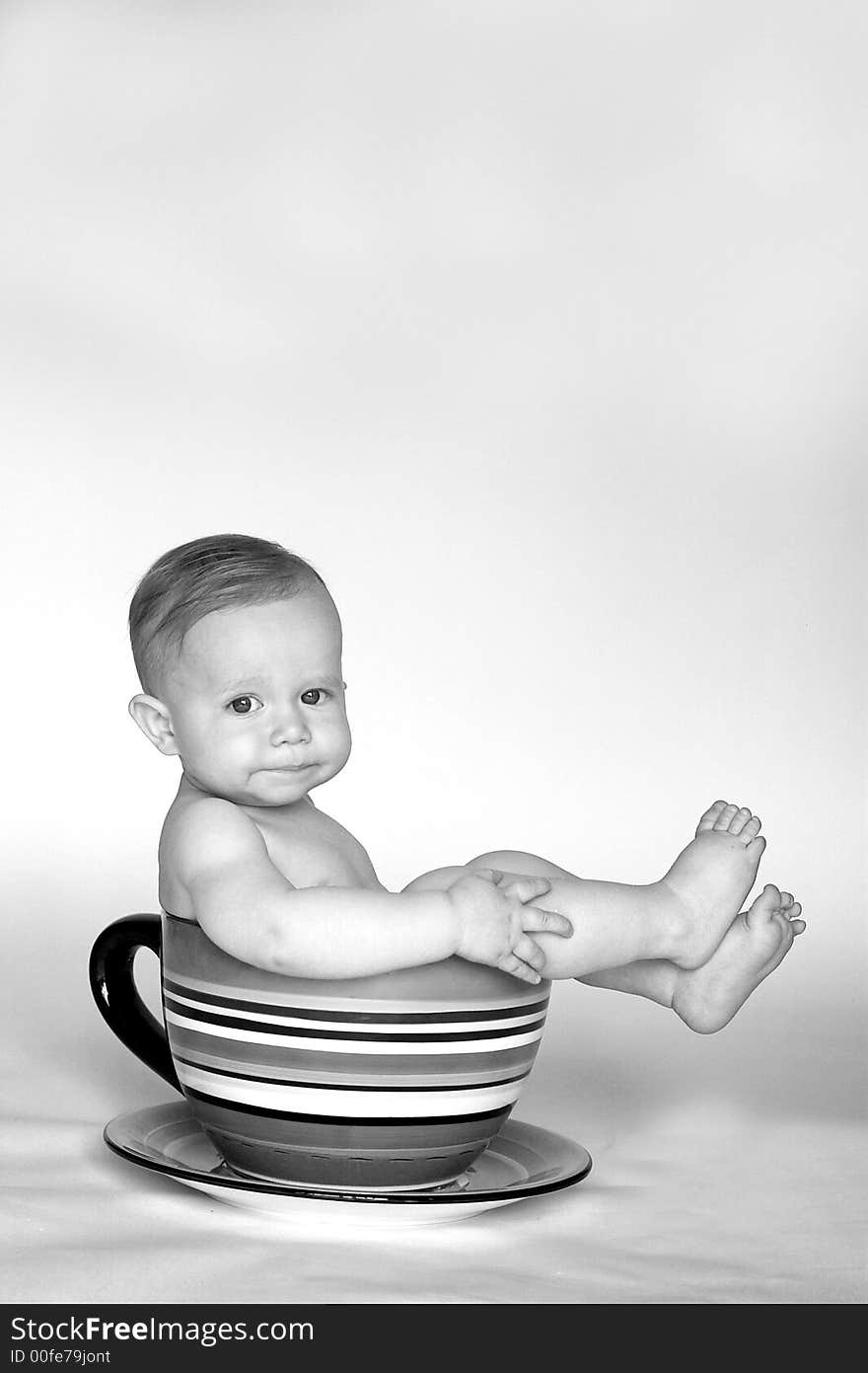 Black and white image of an adorable baby sitting in a colorful, over-sized teacup. Black and white image of an adorable baby sitting in a colorful, over-sized teacup