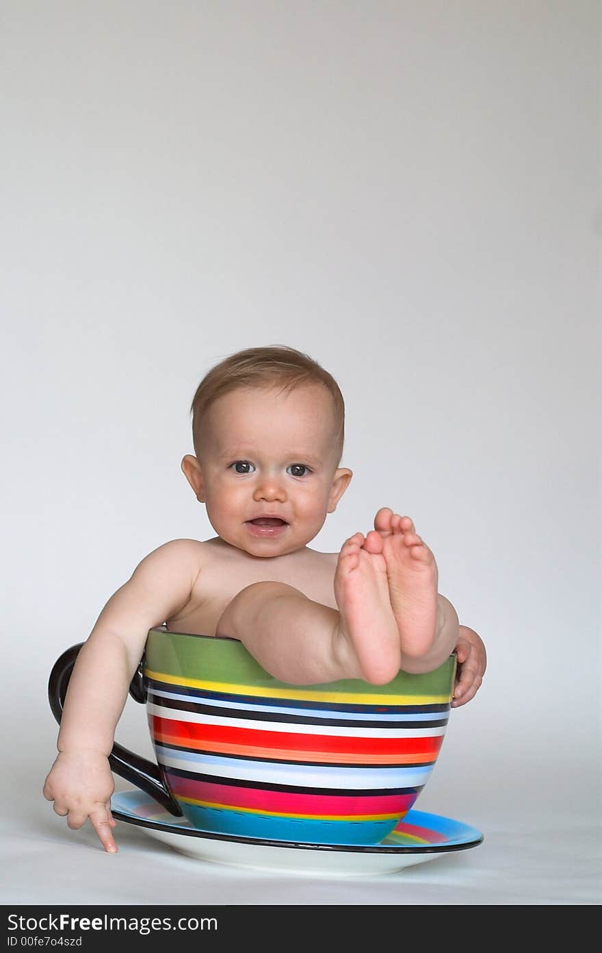 Image of an adorable baby sitting in a colorful, over-sized teacup. Image of an adorable baby sitting in a colorful, over-sized teacup