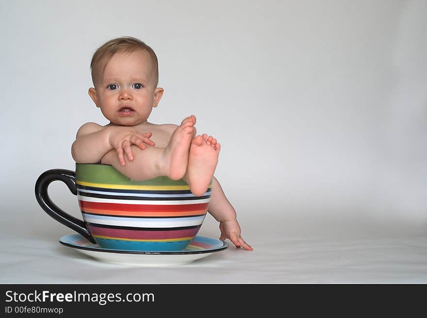 Image of an adorable baby sitting in a colorful, over-sized teacup. Image of an adorable baby sitting in a colorful, over-sized teacup