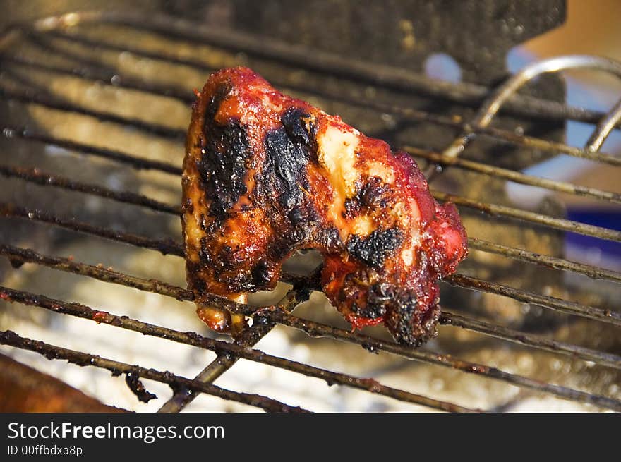 A sizzling piece of tandoori chicken cooks on a barbeque