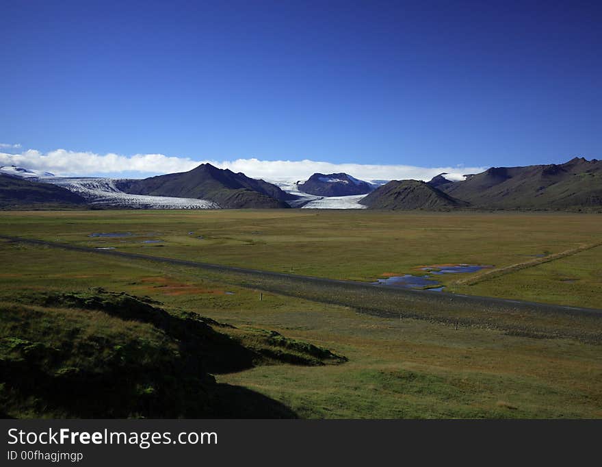 Icelandic Glacier over green fields against a blue sky